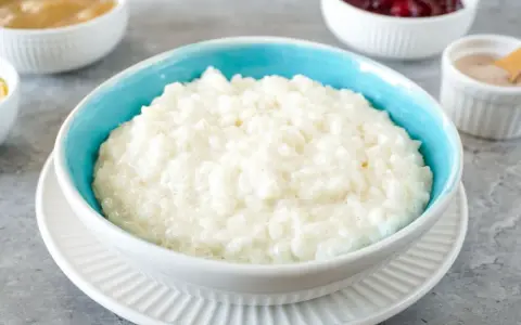 Cremiger Milchreis im blauen Schälchen, daneben Apfelmus, Kirschen und Zimt. Perfekt für ein einfaches Milchreis Rezept.