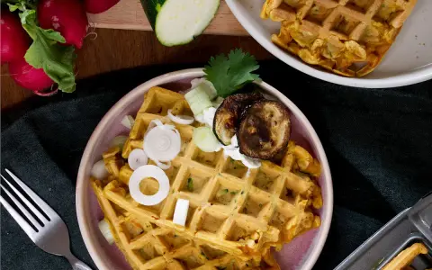 Herzhafte Waffeln mit Zucchini, Zwiebeln und gegrillten Auberginen, garniert mit Kräutern und einem Klecks Joghurt.
