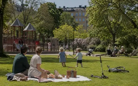 Familj picknickar i parken medan barnen leker. En perfekt dag för aktiviteter i Lund för vuxna och barn.