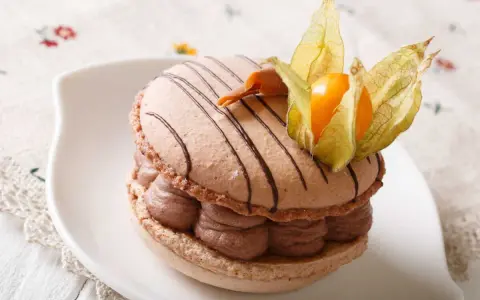 Un macaron chocolat au lait, garni de crème onctueuse et décoré d'une physalis, prêt à être dégusté.