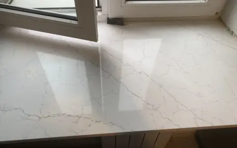 Biały konglomerat z szarymi żyłkami, lśniący po polerowaniu, pod otwartym oknem.