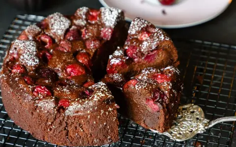 Ein saftiger schoko kirsch kuchen, bestäubt mit Puderzucker, wird auf einem Gitter präsentiert. Eine Gabel hebt ein Stück ab.