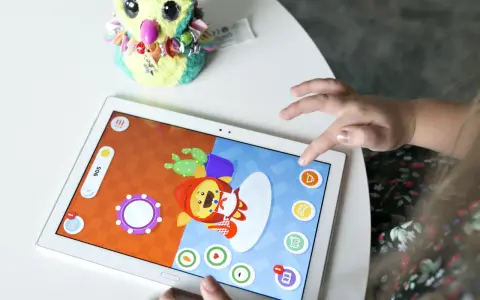 Dziecko gra w gry dla dzieci na telefonie, dotykając ekranu tabletu. Obok leży pluszowa sowa.