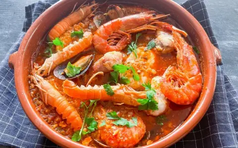 Deliciosa zarzuela de pescado con gambas, mejillones y cigalas en una cazuela de barro, adornada con perejil fresco.