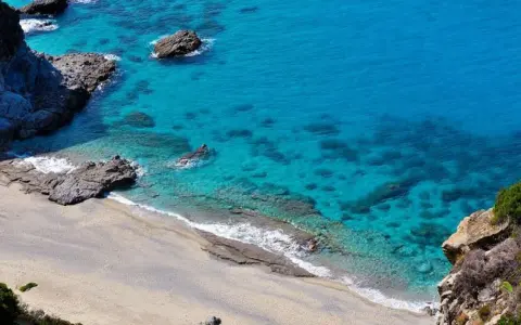 Spiaggia dorata e mare cristallino con scogli a Capo Cozzo.