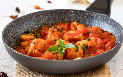 Bocconcini di pollo in padella con pomodoro e basilico, un piatto succulento pronto per essere gustato.