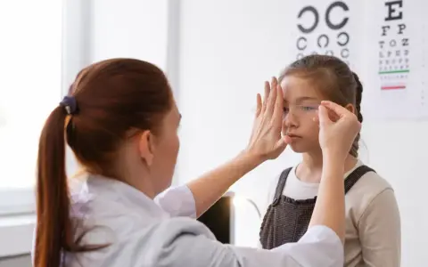 Okulista wykonuje ćwiczenia na akomodację oka u dziewczynki, zasłaniając jej jedno oko.