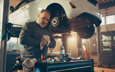 Mechanik wyciera ręce, podczas gdy samochód wisi na podnośniku, odsłaniając układ hamulcowy.