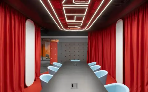 Aménagement salle de réunion moderne avec table noire, fauteuils bleus, rideaux rouges et éclairage néon au plafond.