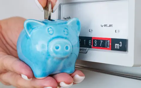 Ahorra con el plan renove calderas gas natural. Una mano deposita una moneda en una hucha cerdito azul junto a un contador de gas.