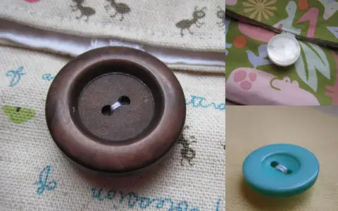 Gros plan sur un bouton à queue marron, prêt à être cousu sur un tissu orné de petites fourmis. Un autre bouton nacré est visible sur un tissu coloré.