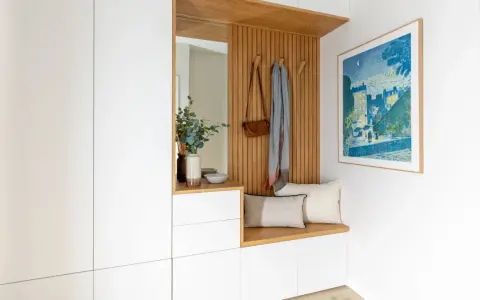 Ideas para decorar recibidor pequeño: banco de madera, espejo, perchero con bolso y bufanda, cuadro y armarios blancos.