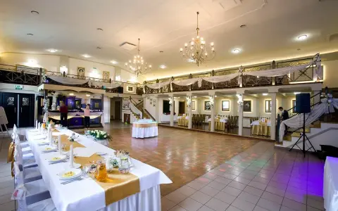 Elegancka sala weselna z długim stołem, ozdobionym złotą podkową. W tle bar i schody prowadzące na antresolę.