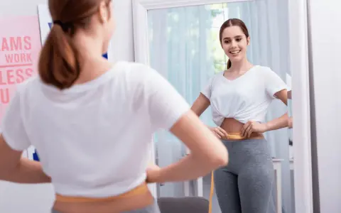 Mujer se mide la cintura con cinta métrica, sonriendo al verse en el espejo. No hay evidencia de que el diu de cobre engorde.