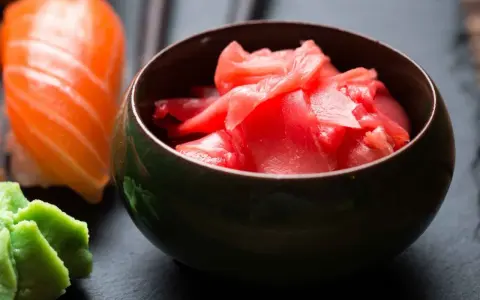 Miseczka z różowym imbirem do sushi, obok kawałek łososia i zielone wasabi.