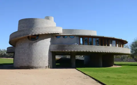 Bâtiment circulaire en béton, exemple des structures conçues par Frank Lloyd Wright, avec des fenêtres rondes et une façade en gradins.