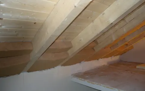 Isolamento tetto dall'interno fai da te: pannelli isolanti in fibra di legno tra le travi di legno grezzo, con sottotetto in perline.