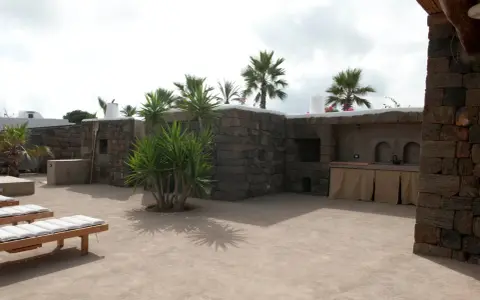 Un cortile in cemento trasformato con piante rigogliose, un barbecue in pietra e comodi lettini. Idee per come abbellire un cortile in cemento.
