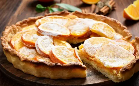 Une délicieuse tarte à l'orange, garnie de fines tranches d'agrumes et saupoudrée de sucre glace, sur un fond de bois rustique.
