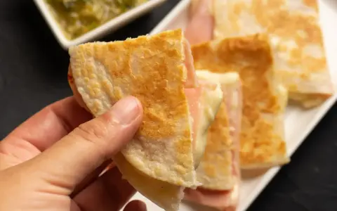 Ciepłe quesadille z szynką i serem, idealne na szybką kolację. Obok sos.