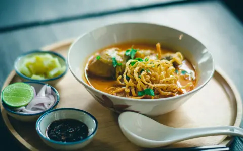 Aromaticzne danie z makaronem, które może być ramen lub udon, podane z dodatkami: limonką, cebulą i pikantnym sosem.