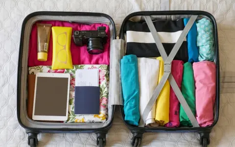 Packar för resan! I det öppna incheckat bagage sas ligger kläder, kamera, solkräm, glasögon, surfplatta och pass.