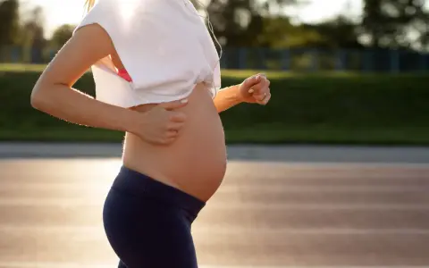 En gravid kvinna springer på en löparbana i solnedgången.