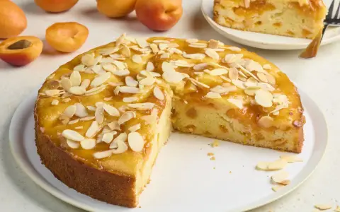 Saftiger aprikosenkuchen mit frischen aprikosen und Mandelblättchen, ein Stück bereits angeschnitten.