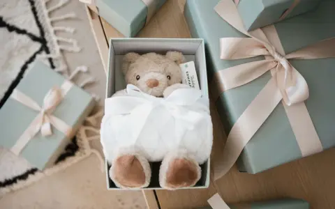 En mjuk nallebjörn i en presentbox, omgiven av fler presenter med ljusrosa band. En perfekt välkommen till världen present.