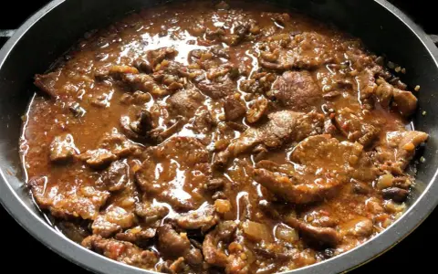 Fricandó de ternera cocinándose en una sartén, con trozos de carne tierna en una salsa espesa y aromática.