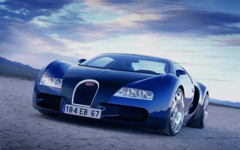 Niebieski Bugatti Veyron na pustynnym tle pod błękitnym niebem.