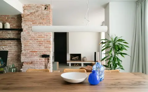 Salón con pared de ladrillo visto, mesa de madera con jarrones y planta.