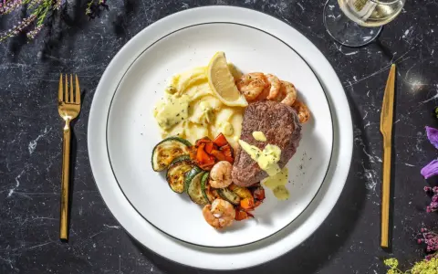 Ein köstliches Surf and Turf Rezept: saftiges Steak, Garnelen, Kartoffelpüree und gegrilltes Gemüse auf einem Teller.