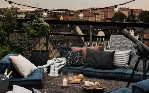 Gemütliche Lounge-Ecke auf einem grossen Balkon mit Blick über die Stadt. Kissen, Decken, Kerzen und ein Teleskop laden zum Entspannen ein.