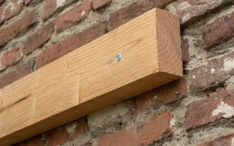 Ein Holzbalken wird mit einer Schraube an einer Ziegelwand befestigt.