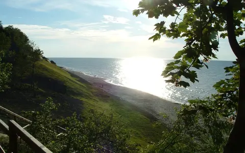 Słoneczny dzień nad morzem, łagodne zbocze porośnięte trawą schodzi do plaży. Jastrzębia Góra atrakcje to spacer po klifie i podziwianie widoków.