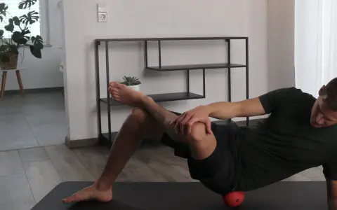 Mann dehnt den Piriformis mit einem roten Ball unter der Hüfte.