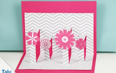 Eine pinke Pop-up-Karte basteln mit Blumen auf grau-weißem Zickzack-Muster.