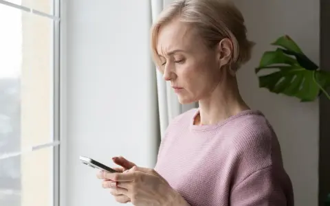Besorgte Frau blickt auf ihr Handy. Sie fragt sich, ob ihr Handy ausspioniert wird.
