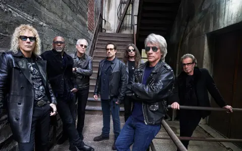 Zespół Bon Jovi gotowy na koncert, w skórzanych kurtkach i okularach przeciwsłonecznych, pozuje na tle industrialnych schodów.