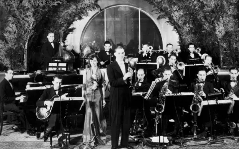 Orkiestra grająca muzykę lat 30. na scenie. Wokalistka w eleganckiej sukni, klarnetysta, gitarzysta i sekcja dęta.