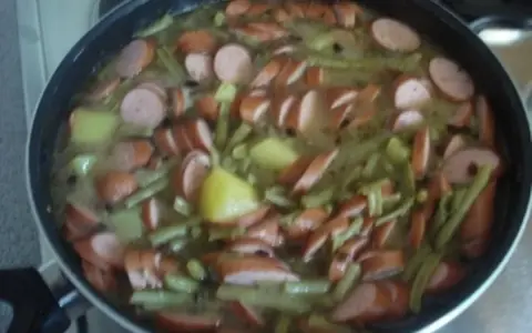 Ein deftiges schnippelbohnen rezept mit Kartoffeln und Würstchen in einer Pfanne.