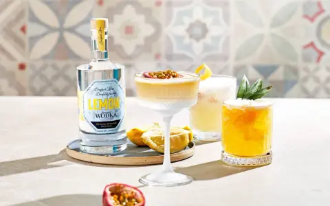 Erfrischender Vodka Sour mit Passionsfrucht und Zitrone, daneben ein weiterer Cocktail mit Ananas. Eine Flasche Zitronen-Wodka steht bereit.