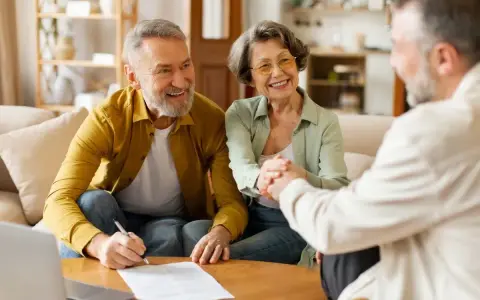 Couple âgé souriant discutant avec un conseiller, signature d'un prêt relais senior.