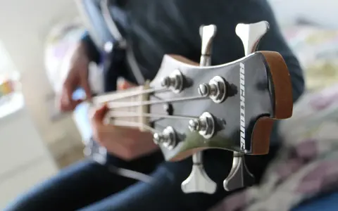 Osoba gra na gitarze basowej, tworząc głębokie akordy basowe.