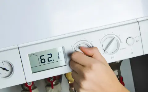 Dłoń reguluje ustawienie pieca gazowego. Na wyświetlaczu 62.1°C, obok manometr i pokrętła regulacji.