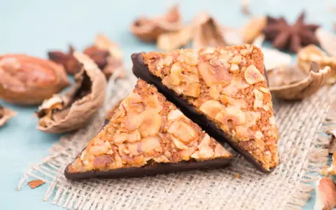 Zwei dreieckige Nussecken mit Schokoladenboden, bestreut mit gehackten Nüssen. Ein köstliches nussecken rezept zum Nachbacken.