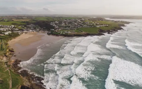 Aerial videography captures a coastal village with a sandy beach and rolling waves.