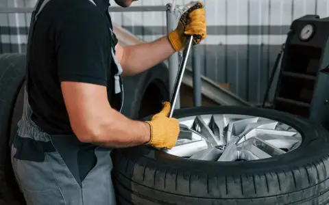 Mechanik w żółtych rękawicach używa klucza, by pokazać, jak zdjąć oponę z felgi.