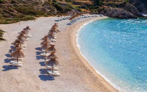 Rządki parasoli i leżaków na kamienistej plaży, obok krystalicznie czystej, turkusowej wody. To jedna z najpiękniejszych plaż w Europie, idealna na relaks.